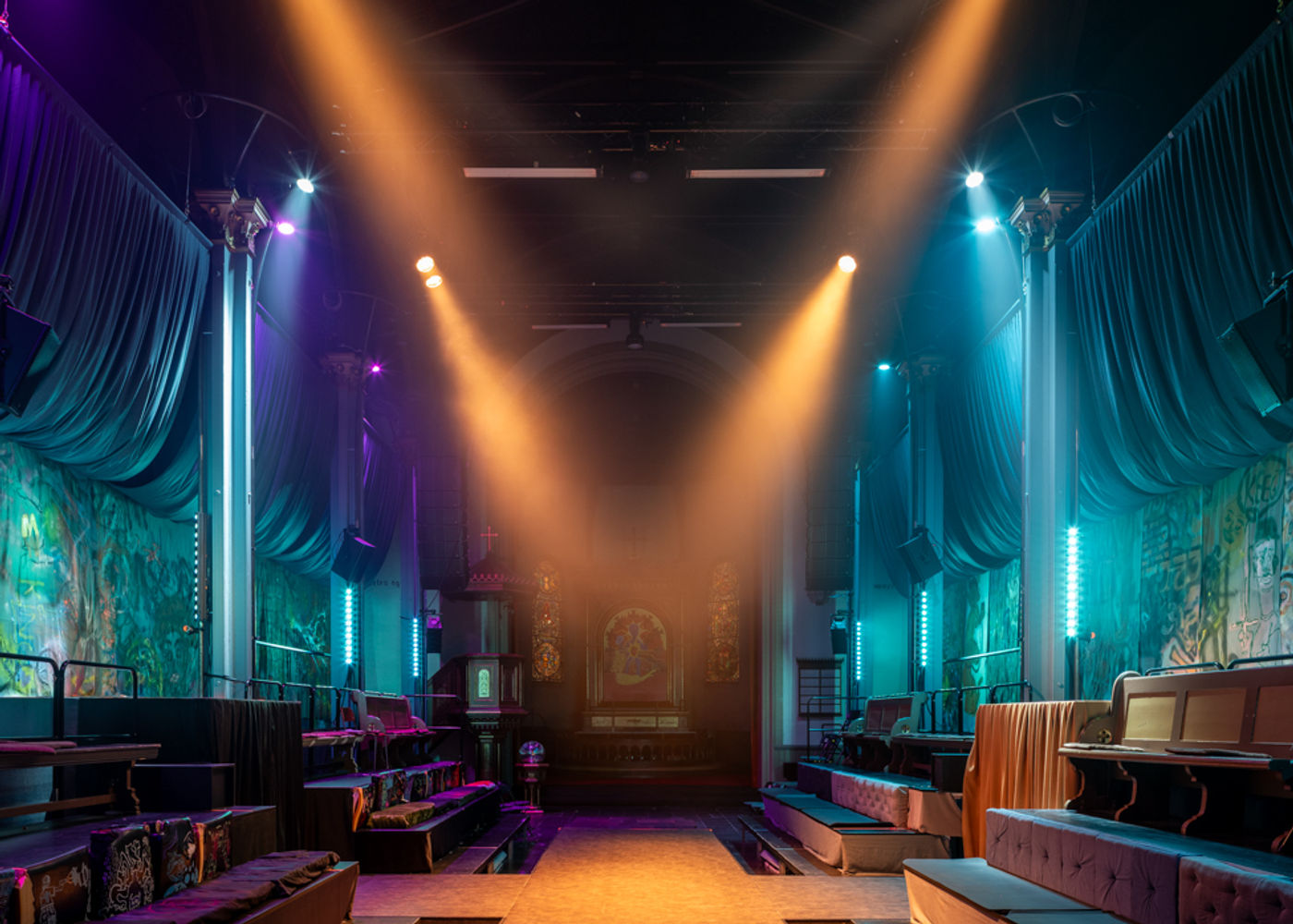 A runway stage set across the church nave — stage design for Tigerstadsteatret’s Romeo and Juliet, Oslo East/West, held between cast-iron trusses and stained glass.
